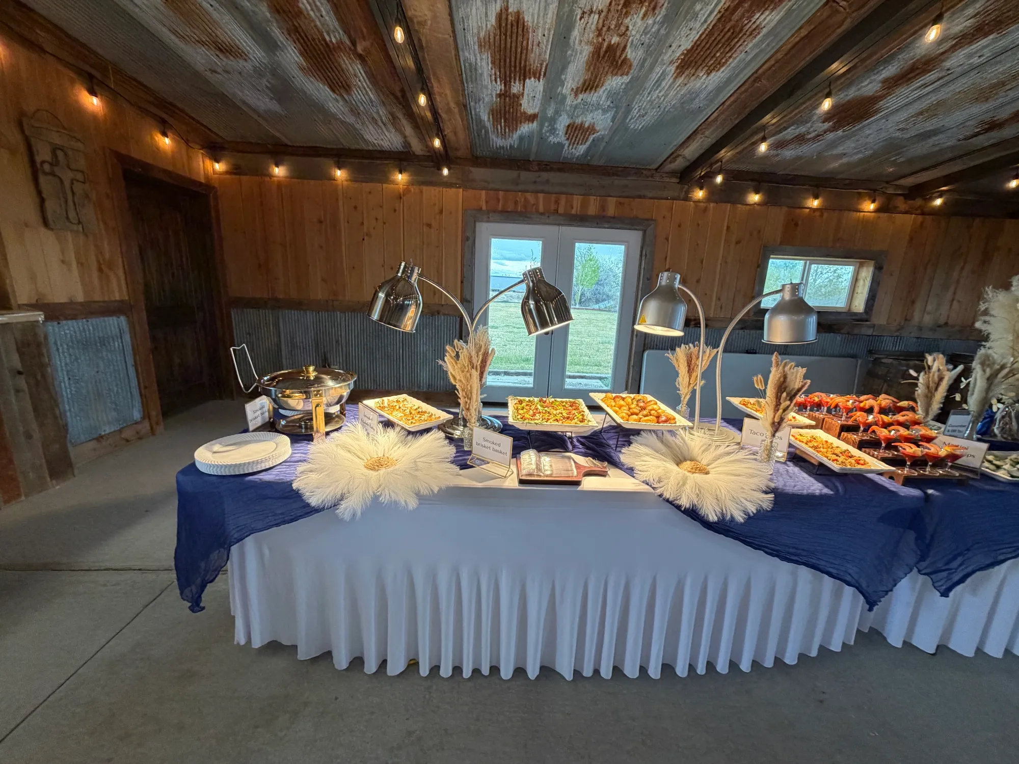 A round table laid for a reception, lit warm against a timber hall.