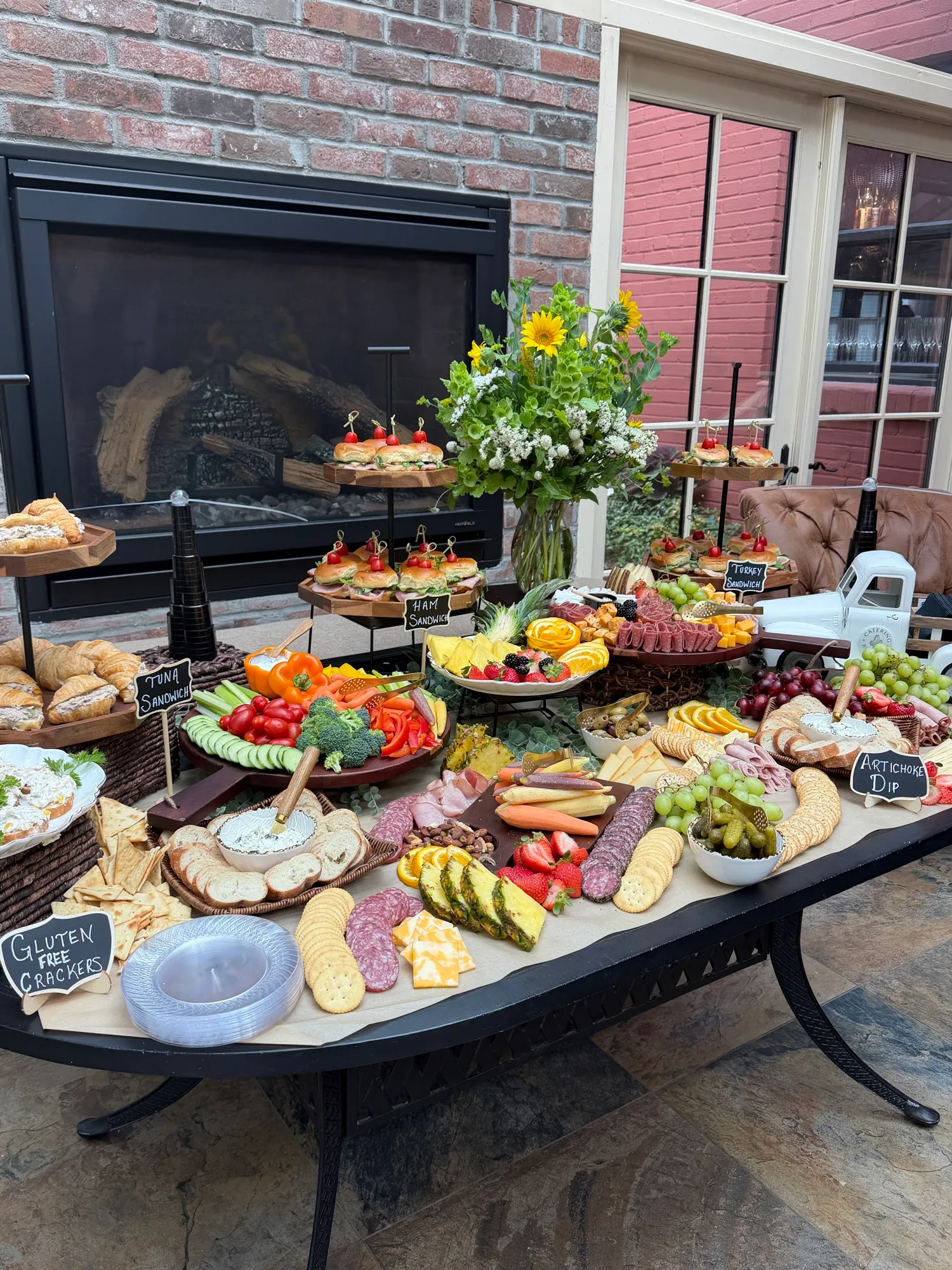 A long grazing table set outdoors with boards of meats, cheeses and vegetables.