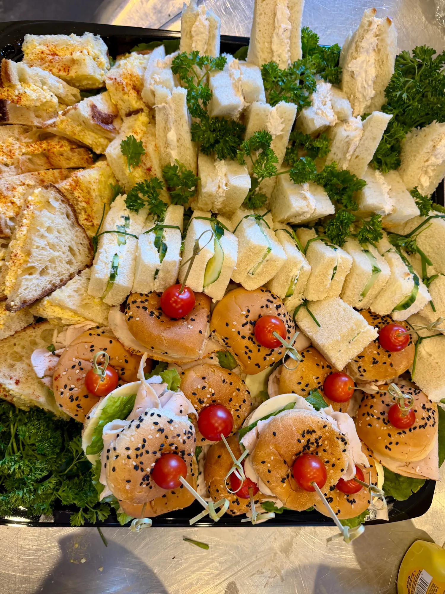 Finger sandwiches and sliders arranged in rows on a serving board.