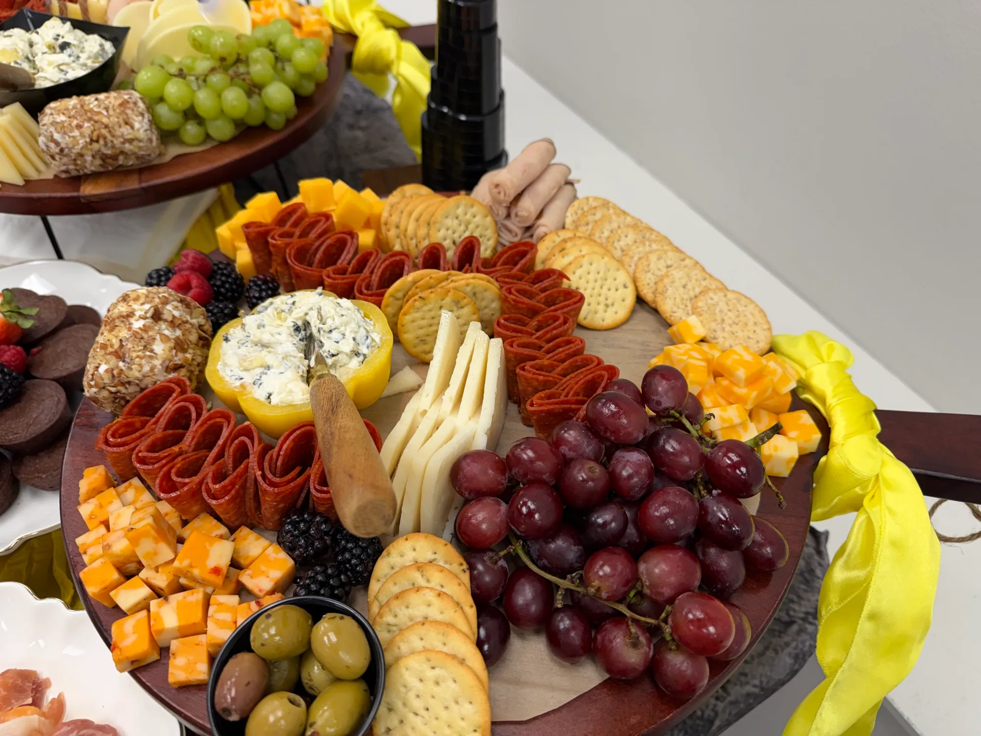 A round charcuterie board with cubed cheeses, olives, grapes and crackers.