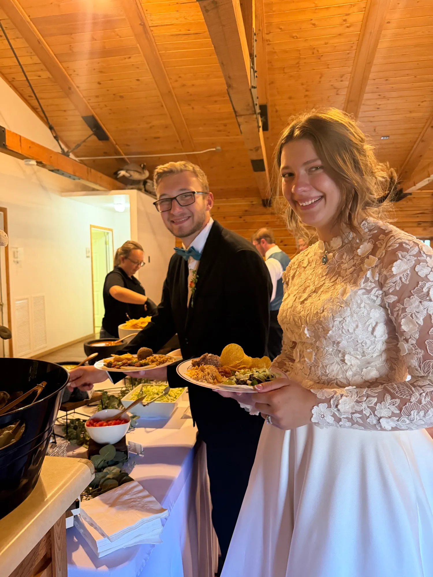 A bride and groom carrying plates away from the buffet.