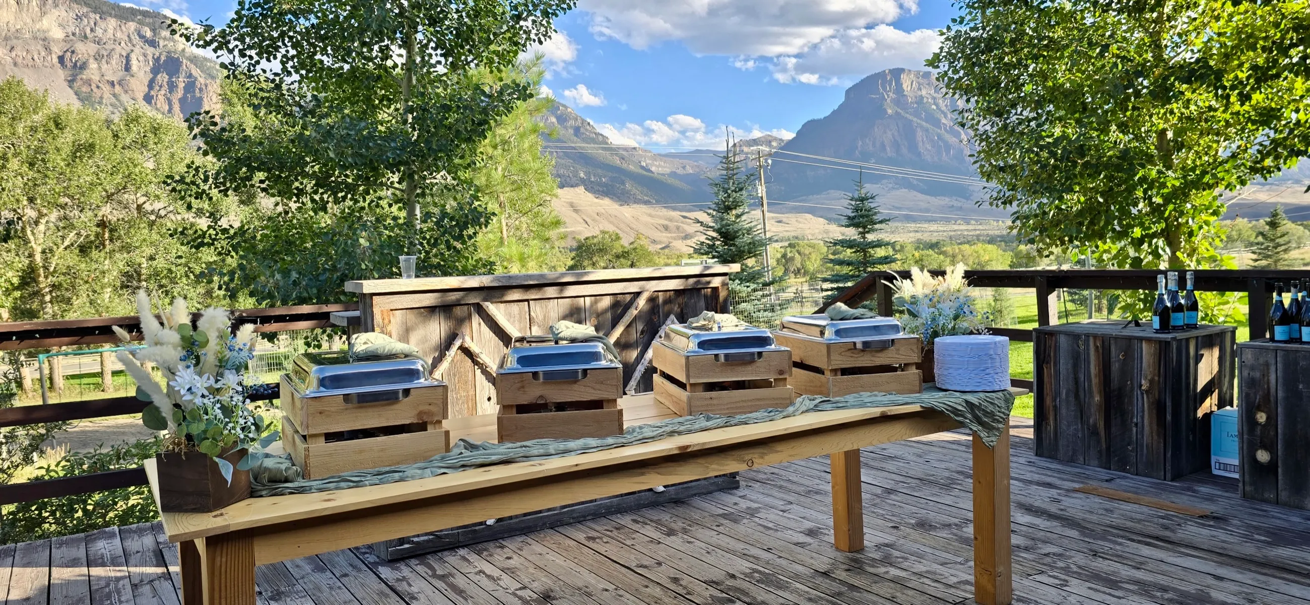 A long buffet table set for an outdoor event, with the Cody foothills rising behind it.
