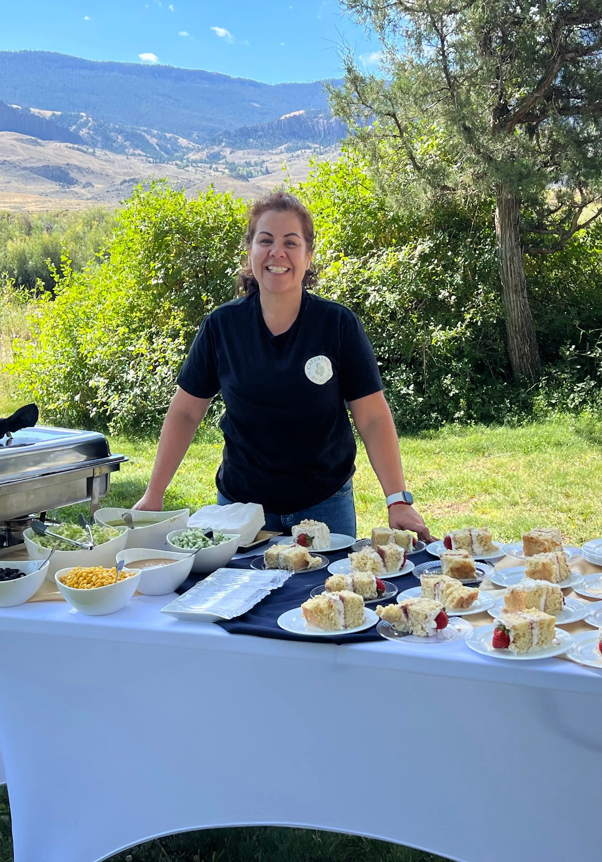 Rosie Roberson behind a dessert table set up outdoors, the Cody foothills behind her.